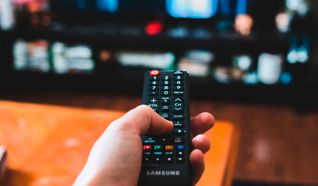 Una mano sostiene un mando a distancia ante el monitor de una televisión.