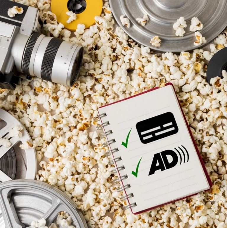Sobre una capa de palomitas de maíz y películas de cine alrededor hay una libreta con los iconos dibujados del subtitulado y de la audiodescripción.