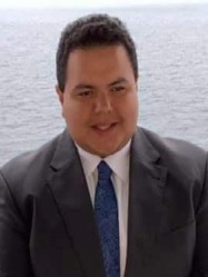 Primer plano de Anthony Quispe con pelo corto moreno, traje oscuro, camisa blanca y corbata azul.