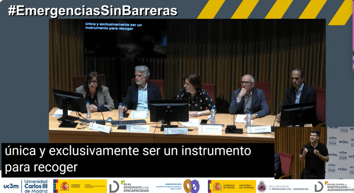 Captura de pantalla del streaming. Sobre fondo gris, como título aparece el hastag #EmergenciaSinBarreras.
Una gran imagen central con los ponentes sentados tras una mesa de madera y tras ellos una pantalla que retransmite los subtítulos.
De izquierda a derecha, Belén Ruiz, Vicente Medrando, Eva María Blázquez, Fernando Prieto e Israel González.
En el bajo los subtítulos en una caja negra y letra blanca y en la esquina inferior derecha hay una ventana con el intérprete de lengua de signos.
